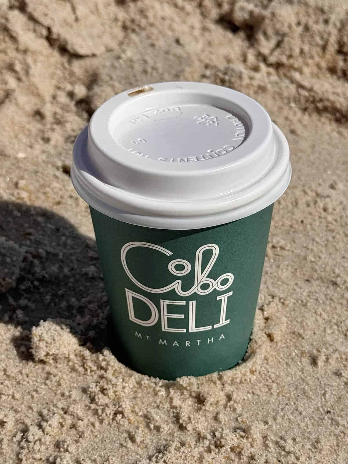 An image of a takeaway coffee from Cibo Deli in Mount Martha wedged into the sand