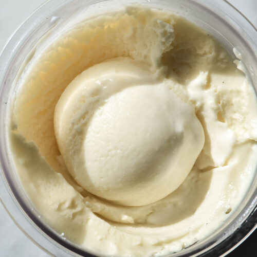 A close up macro aerial image of a tub of Ninja Creami sugar free vanilla ice cream. The ice cream has a scoop in the centre.