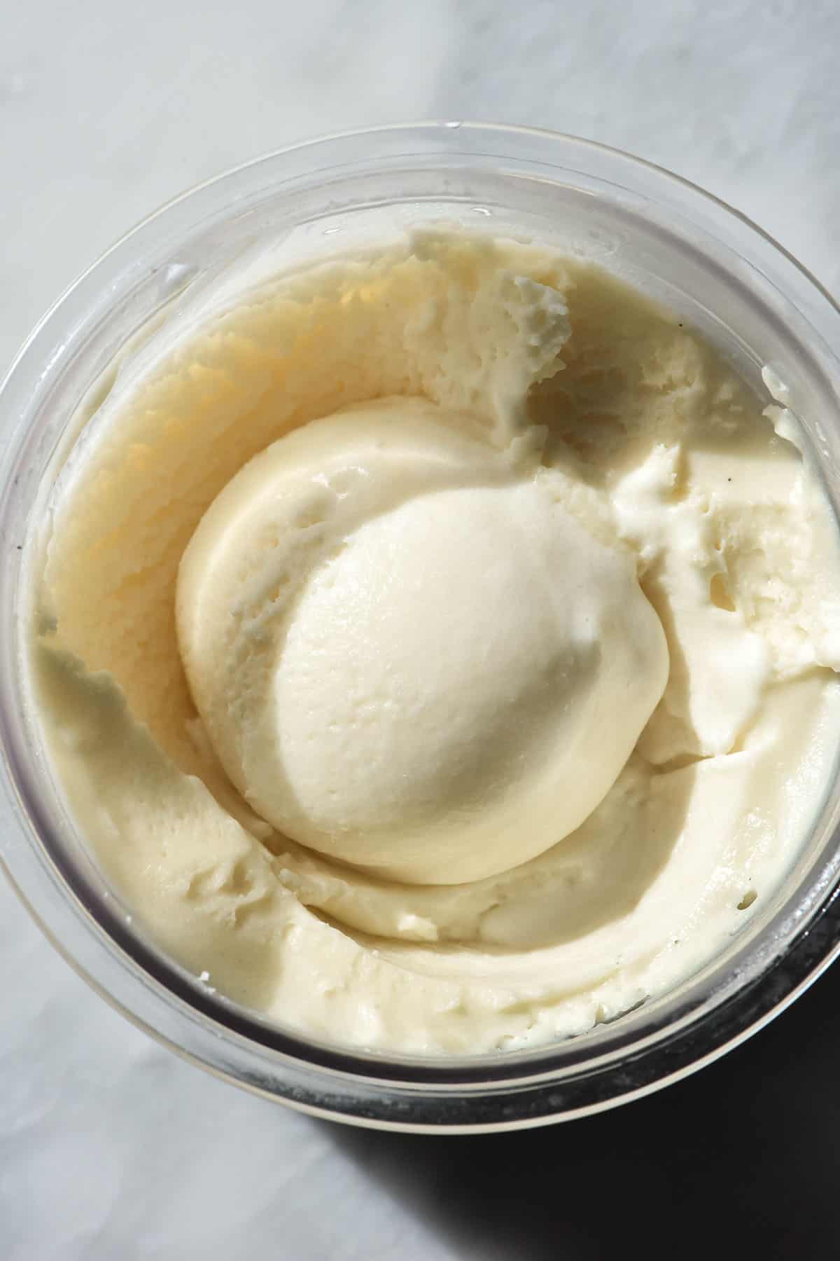 A close up macro aerial image of a tub of Ninja Creami sugar free vanilla ice cream. The ice cream has a scoop in the centre.