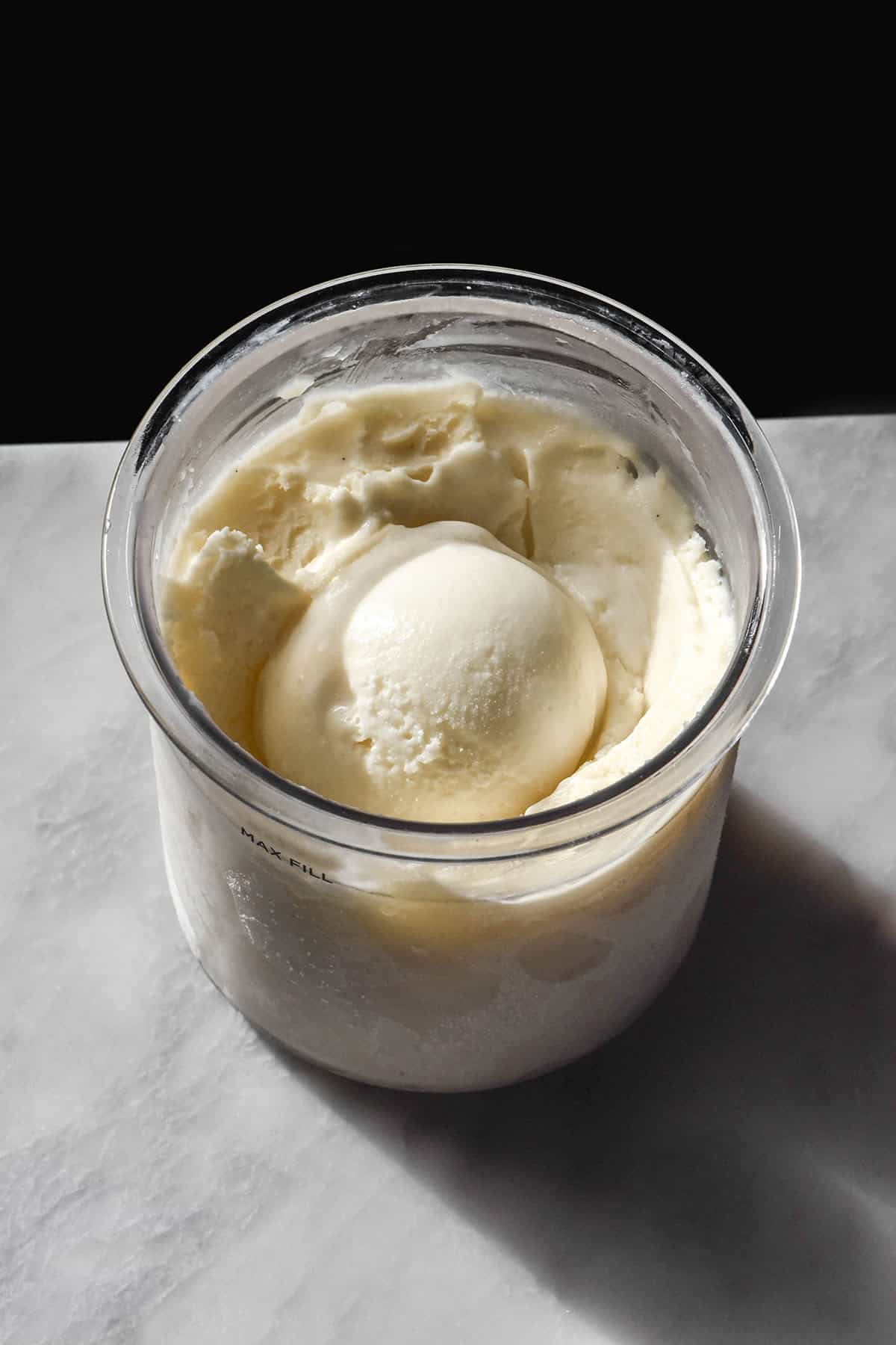 An aerial image of a tub of sugar free vanilla Ninja Creami ice cream on a white marble table against a black backdrop