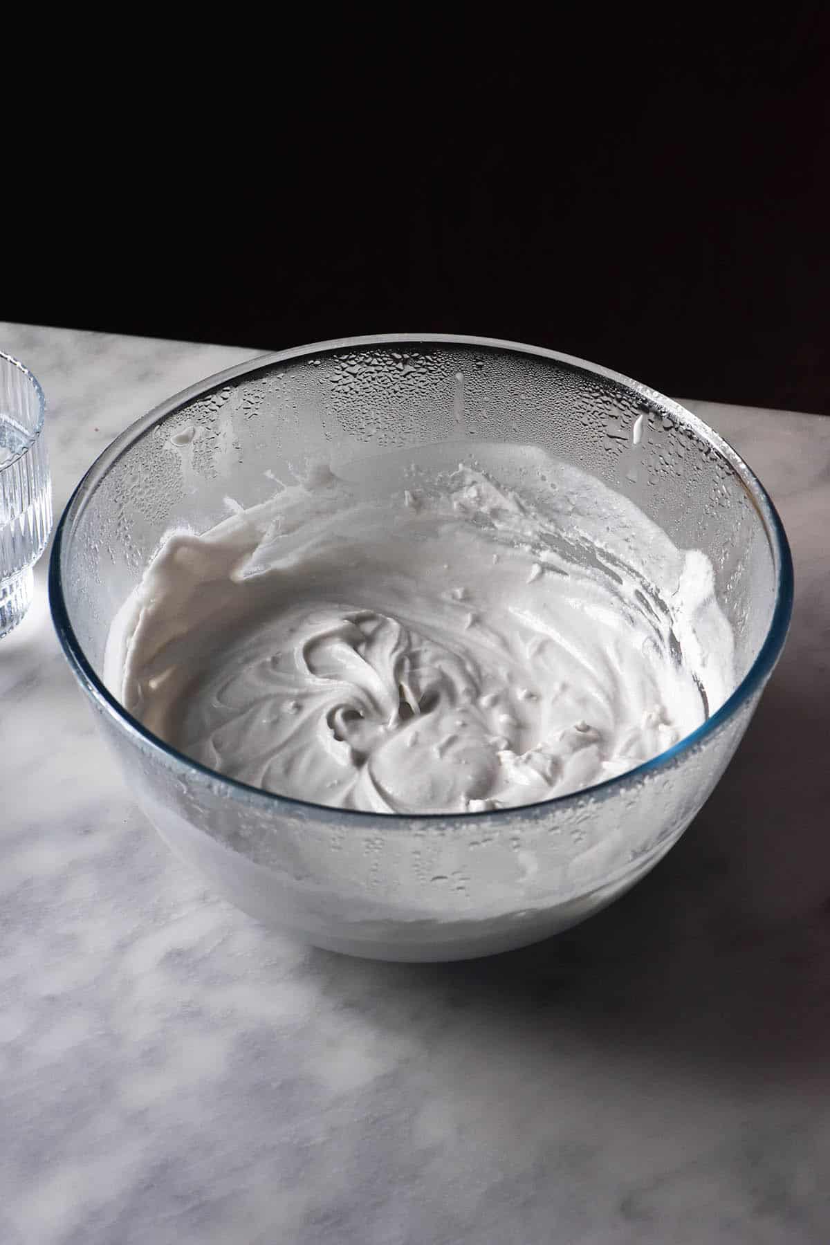 A side on image of a bowl of freshly made homemade coconut yoghurt. The bowl sits atop a white marble table against a black backdrop.
