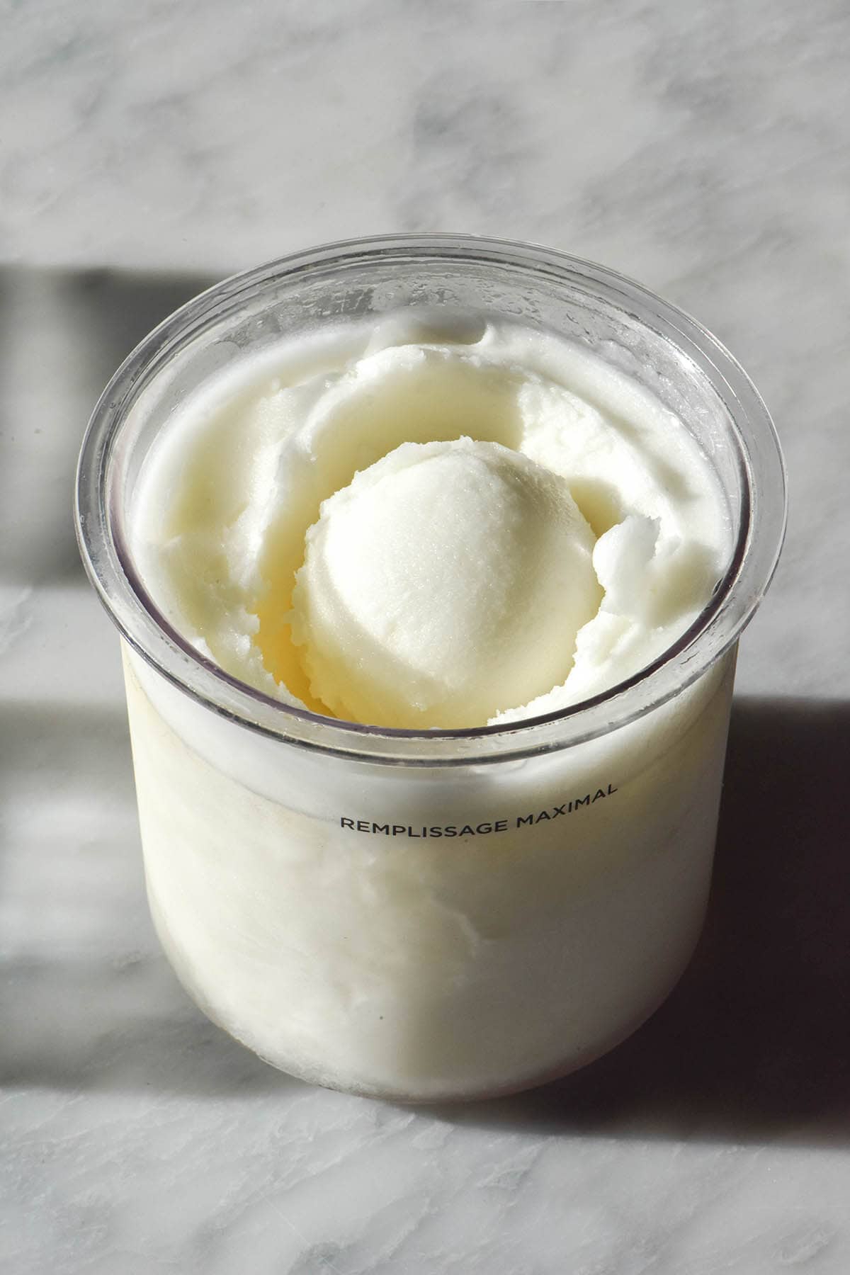 An aerial image of a tub of Ninja Creami lemon sorbet on a sunlit white marble table. The tub has a scoop of sorbet in the middle.