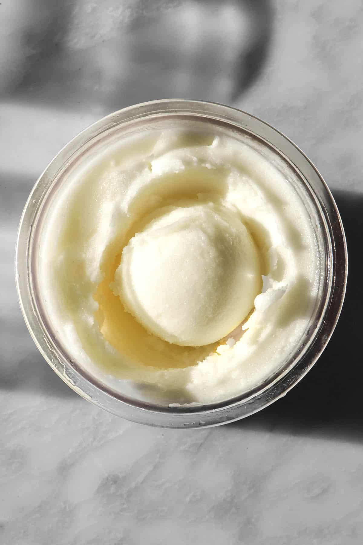 An aerial image of a tub of Ninja Creami lemon sorbet on a sunlit white marble table. The tub has a scoop of sorbet in the middle.