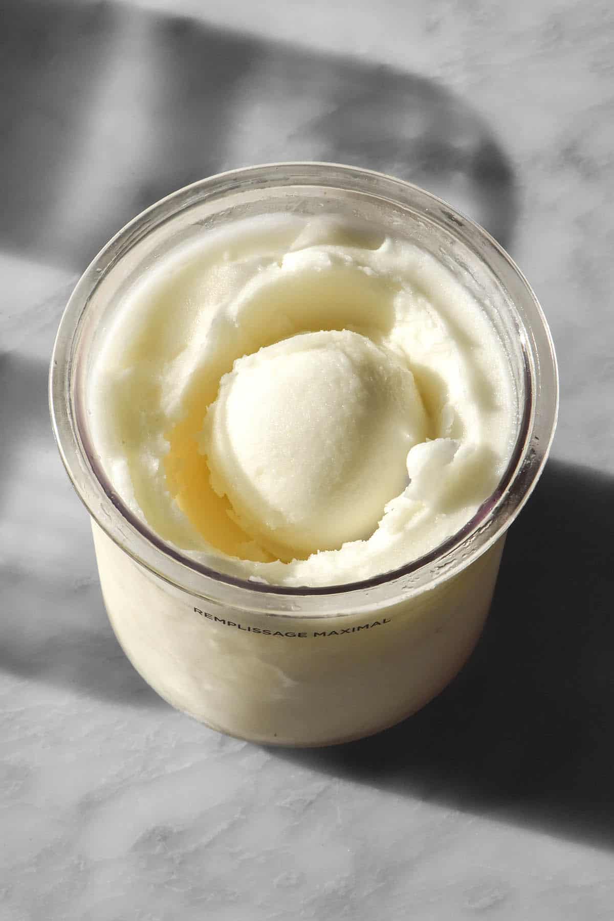An aerial image of a tub of Ninja Creami lemon sorbet on a sunlit white marble table. The tub has a scoop of sorbet in the middle.