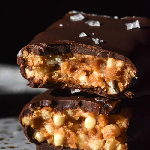 A macro side on image of a protein crisp bar that has been sliced in half and stacked on a white speckled ceramic plate
