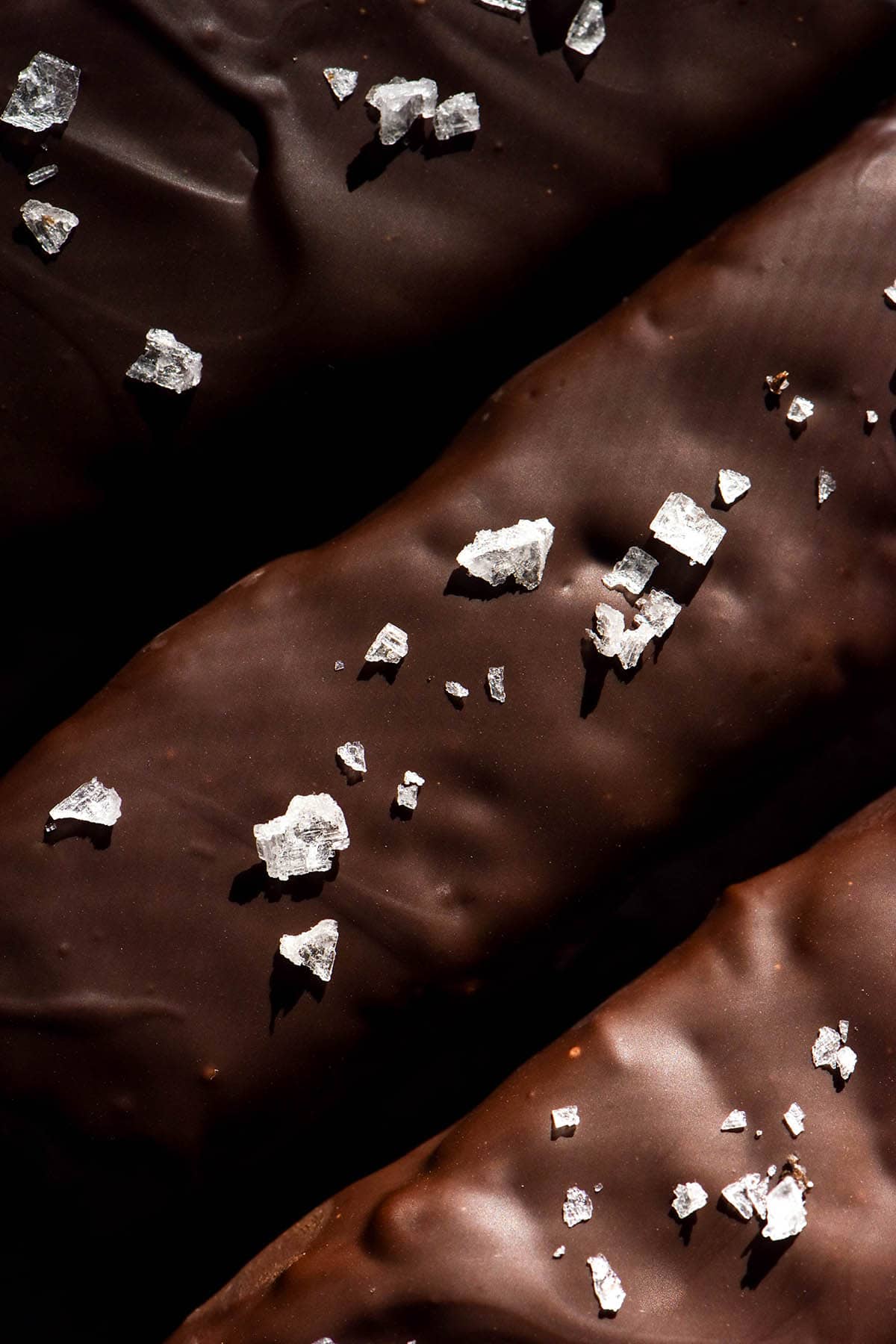 An aerial macro image of three chocolate covered protein crisp bars topped with sea salt flakes