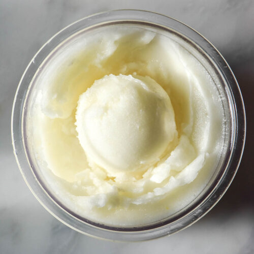 An aerial image of a tub of sugar free Ninja Creami lemon sorbet on a white marble table