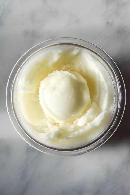 An aerial image of a tub of sugar free Ninja Creami lemon sorbet on a white marble table