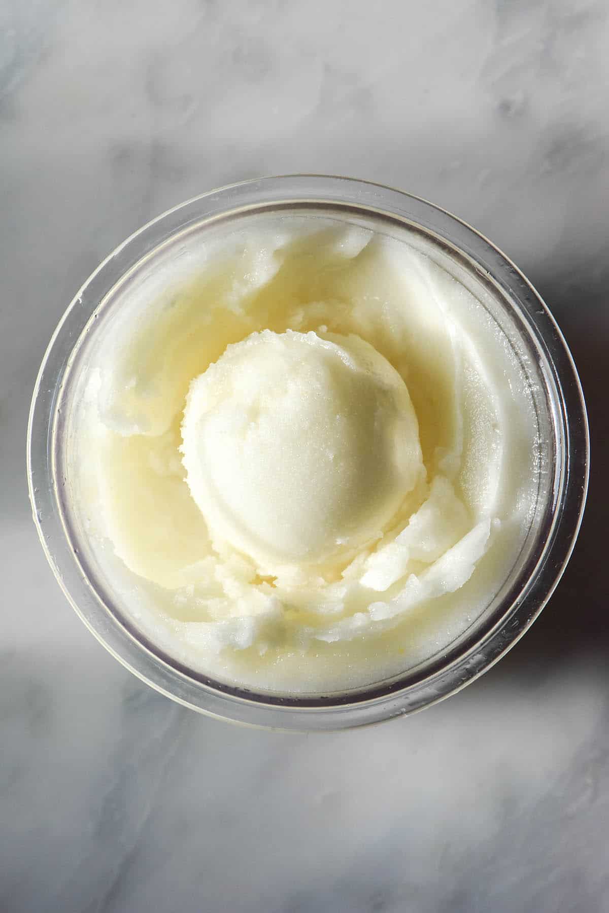 An aerial image of a tub of sugar free Ninja Creami lemon sorbet on a white marble table