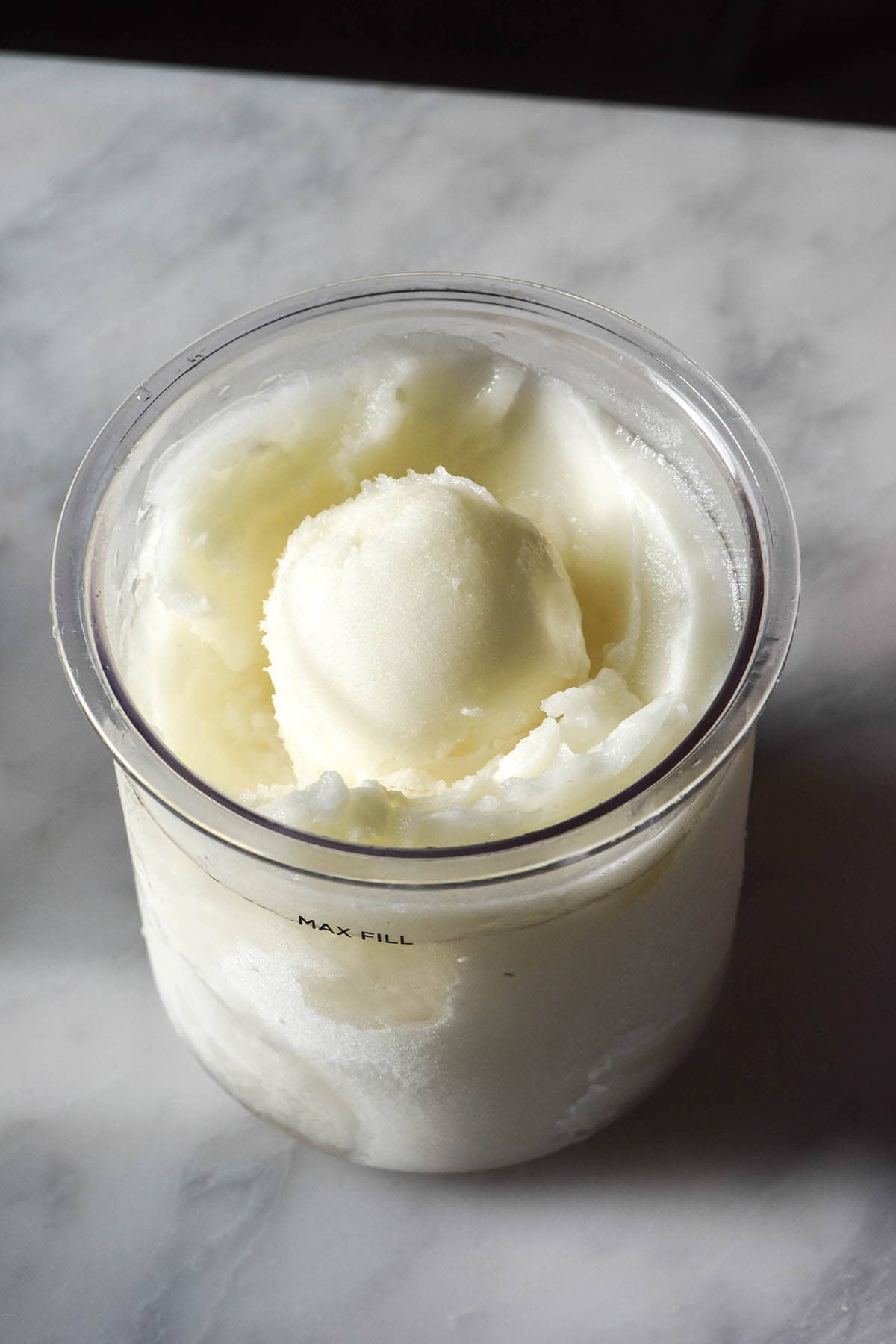A side on image of a tub of sugar free Ninja Creami lemon sorbet on a white marble table against a black backdrop