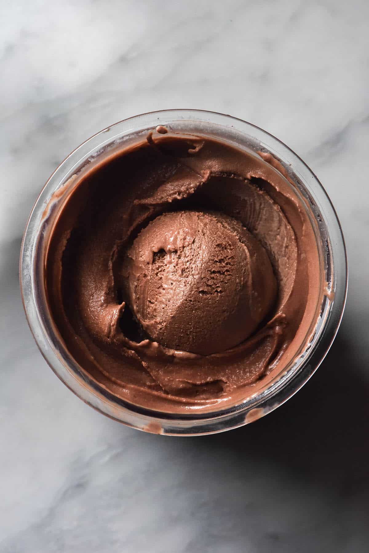 An aerial image of a tub of Ninja Creami sugar free chocolate ice cream on a white marble table.