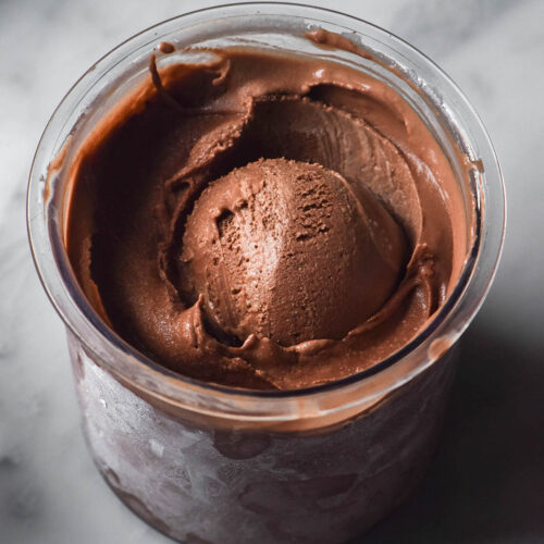 An aerial image of a tub of sugar free chocolate ice cream in a Ninja Creami tub on a white marble table.