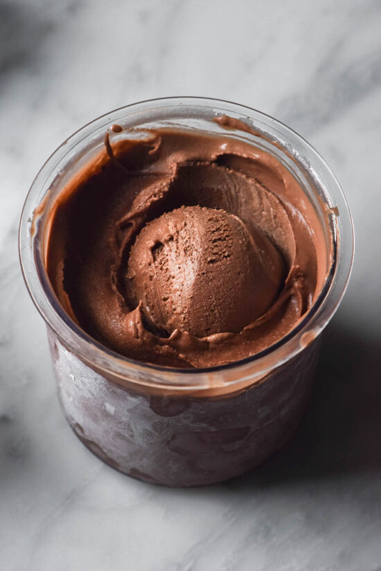 An aerial image of a tub of sugar free chocolate ice cream in a Ninja Creami tub on a white marble table.