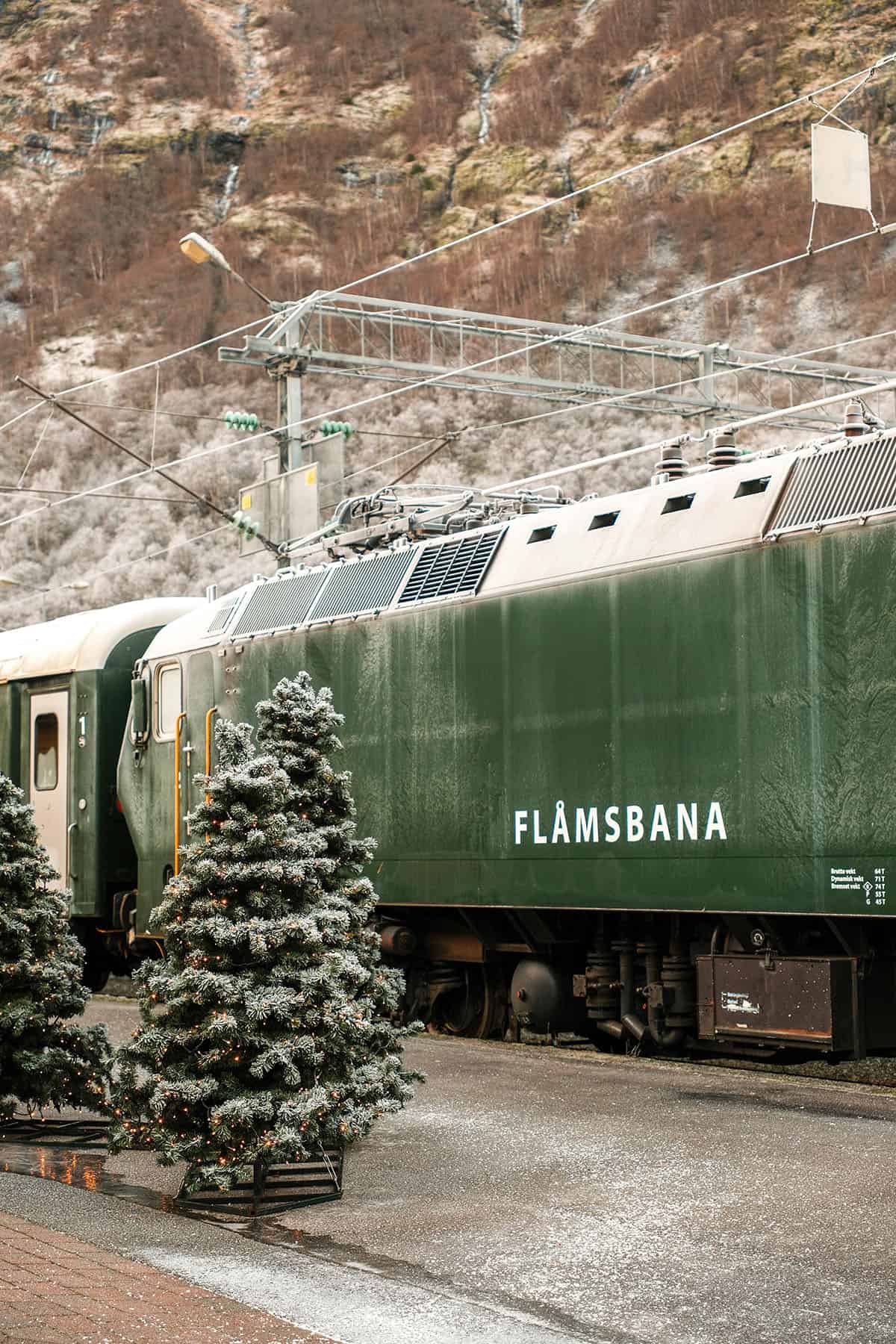 An image of a snow capped Flåmsbana train with a Christmas tree in front of it at Flåm station