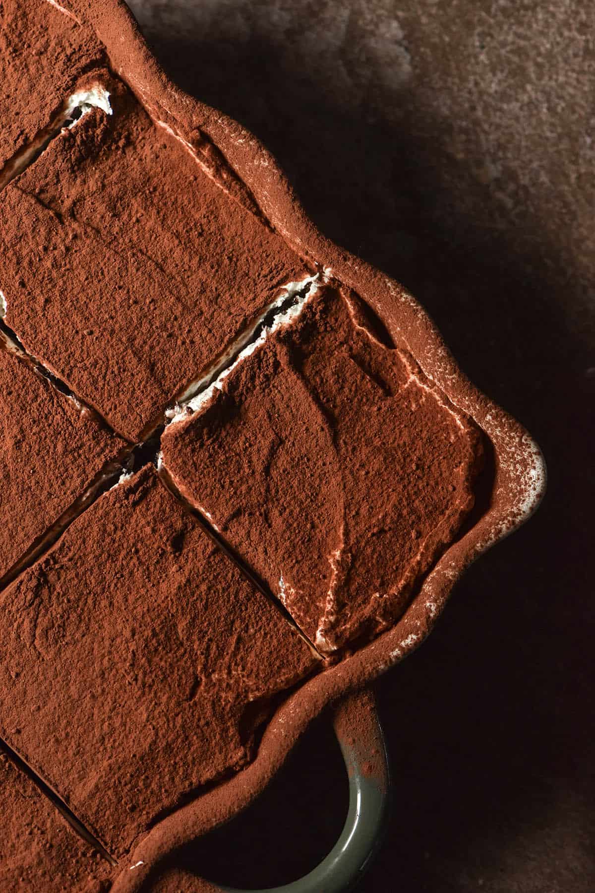 An aerial macro image of a gluten free Oreo tiramisu topped with cocoa. The tiramisu sits atop a dark brown backdrop.
