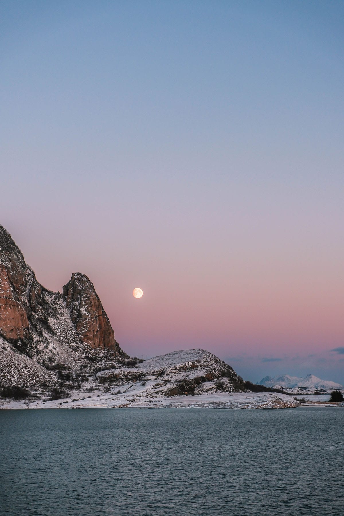 A pink sunset with the moon in the sky on a winter day sailing the coast of Norway on the Hurtigruten