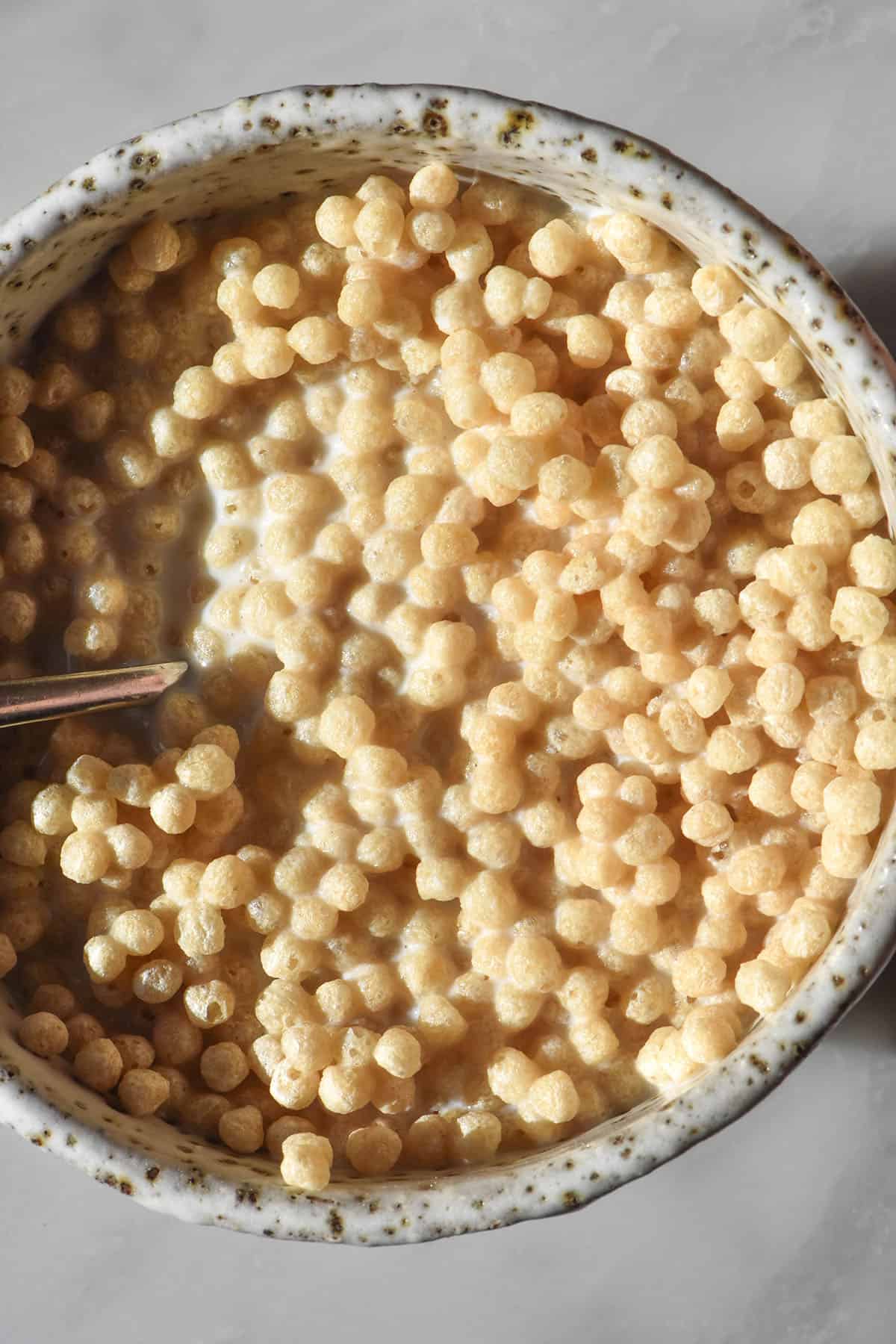 An aerial image of a small ceramic white speckled dish filled with soy protein crisp cereal atop a white marble table
