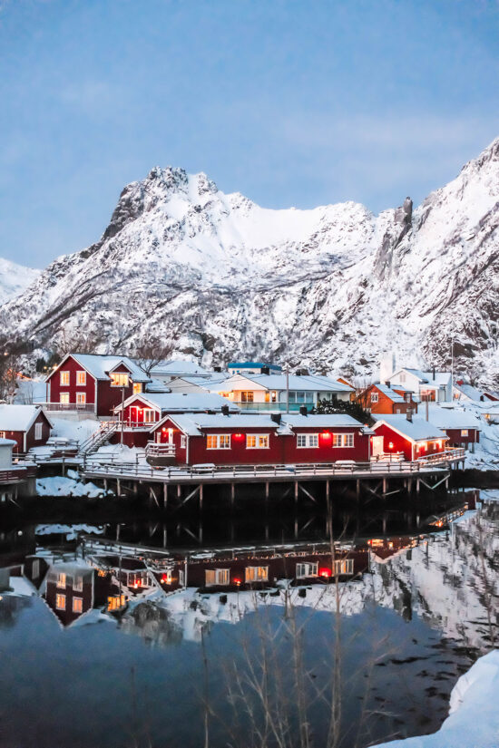 An image of the rorbu of Svolvær set against a snowy backdrop on a clear afternoon