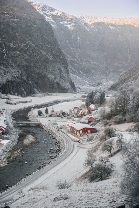 An image of the Flåm church and valley as seen from the Flåmsbana train in December. The valley is capped with snow.