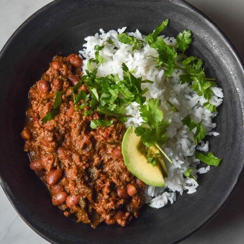 An aerial image of a dark blue bowl filled with low FODMAP chilli con carne atop a white marble table.