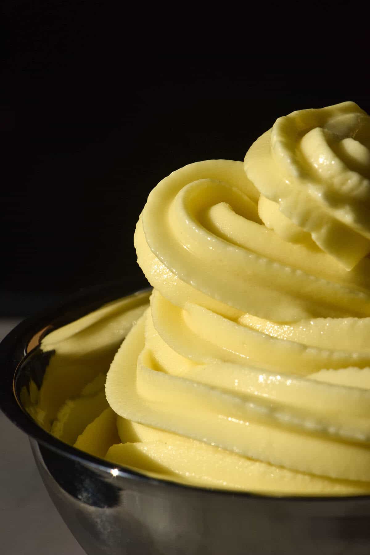 A close up image of a swirl of Ninja Swirl Dole whip in a silver dessert coupe against a dark backdrop