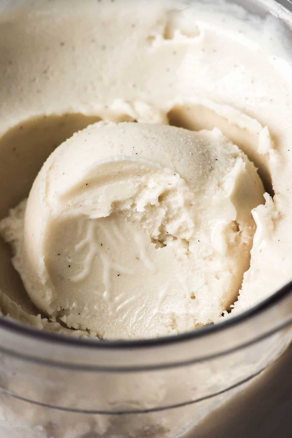 A close up macro image of a scoop of Ninja Creami cashew ice cream that has had a spoonful removed, revealing the creamy texture of the ice cream