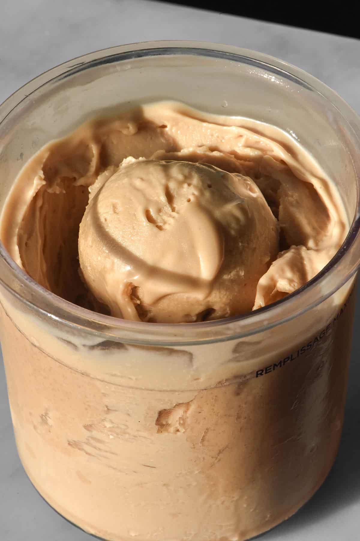 A side on image of a tub of Ninja Creami roasted cashew ice cream on a white marble table
