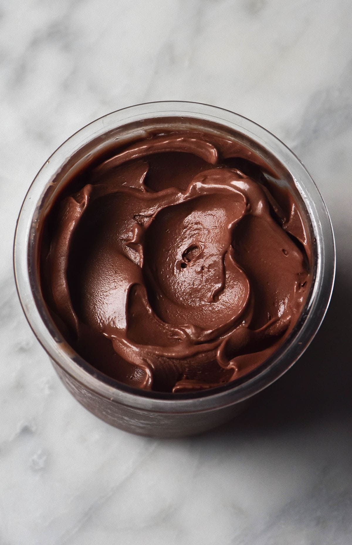 An aerial image of a tub of Ninja Creami vegan chocolate ice cream on a white marble table