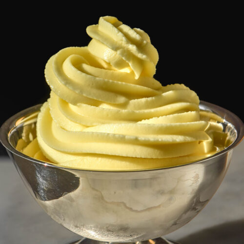 A close up side on image of Ninja Swirl Dole whip in a silver dessert coupe. The coupe sits on a white marble table against a dark backdrop.