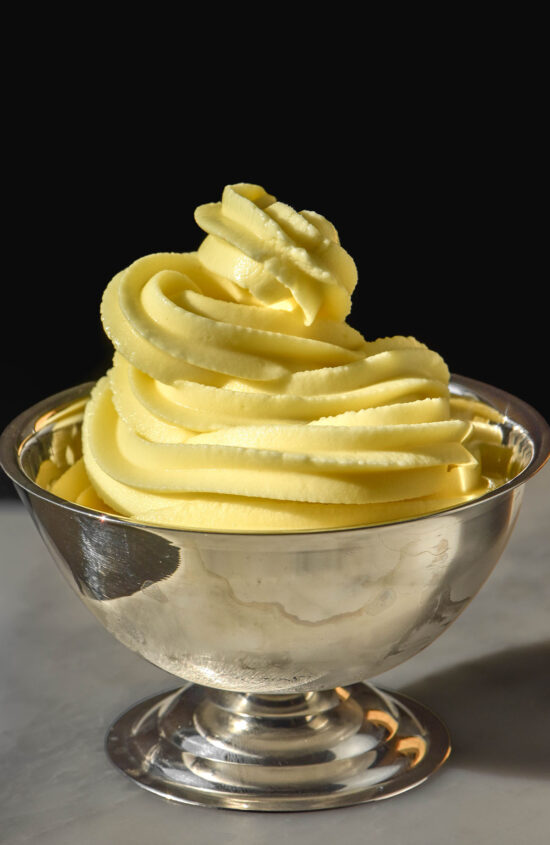 A close up side on image of Ninja Swirl Dole whip in a silver dessert coupe. The coupe sits on a white marble table against a dark backdrop.