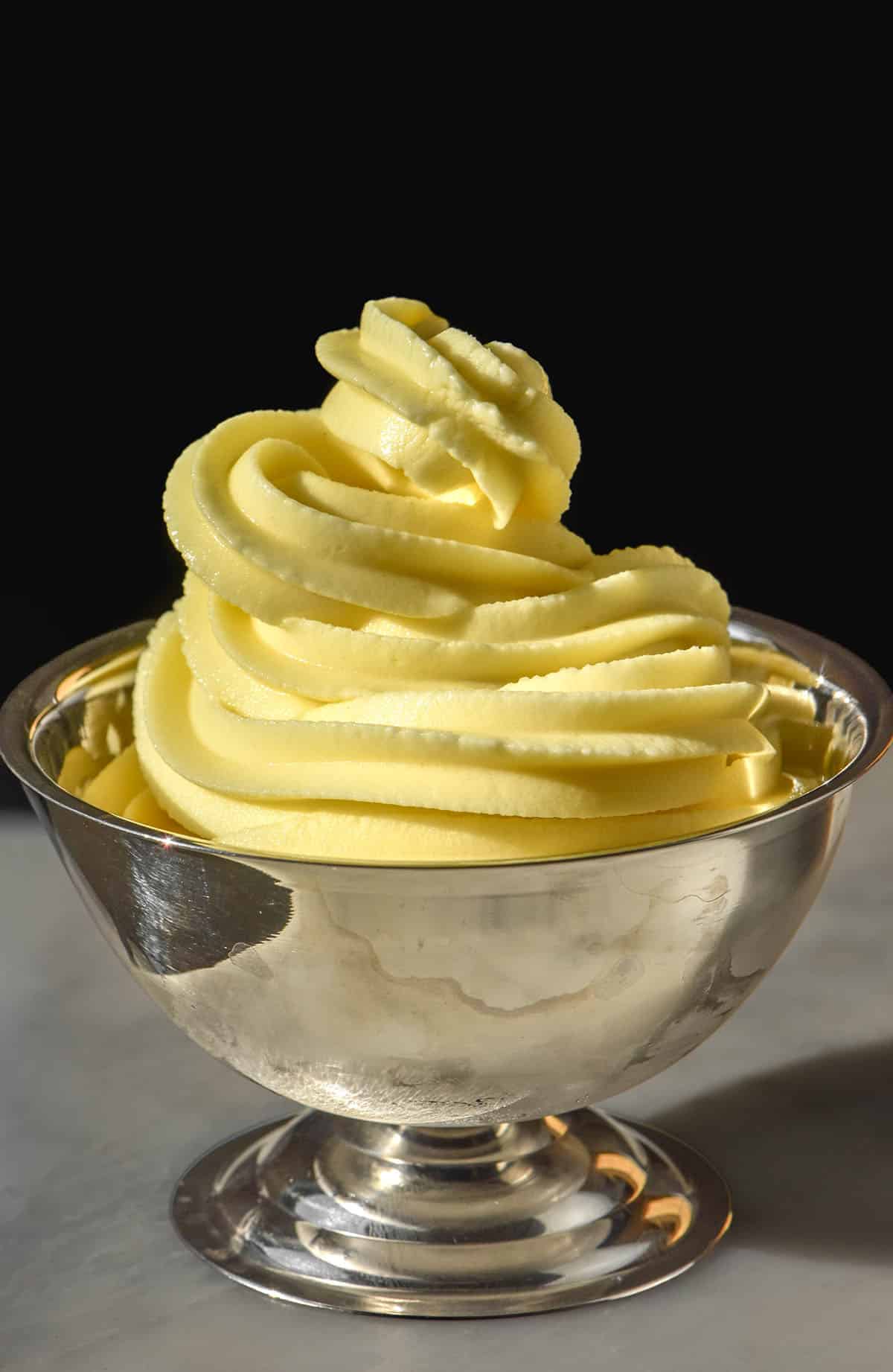A close up side on image of Ninja Swirl Dole whip in a silver dessert coupe. The coupe sits on a white marble table against a dark backdrop.