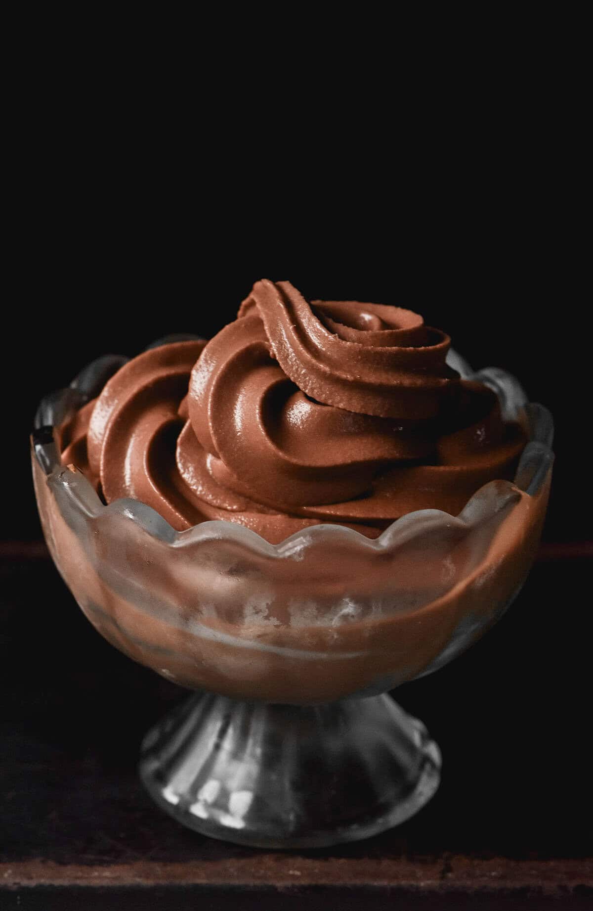 A moody image of a glass scalloped dessert coupe filled with Ninja Swirl chocolate soft serve against a dark backdrop