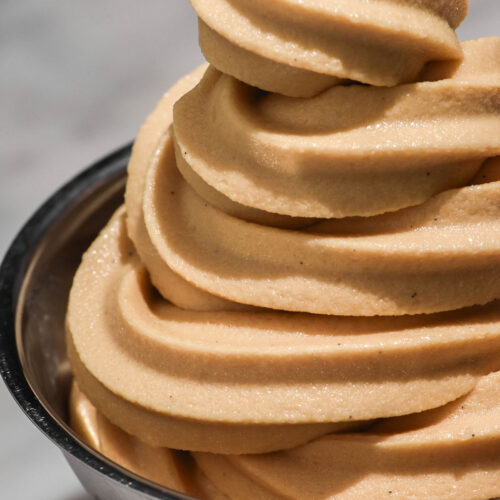 A close up image of a swirl of Ninja Swirl coffee soft serve in a silver dessert coupe on a white marble table