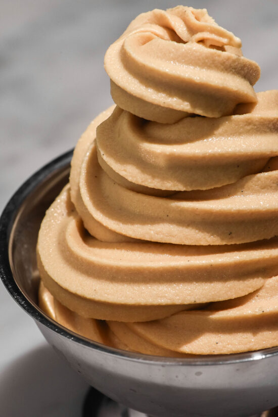 A close up image of a swirl of Ninja Swirl coffee soft serve in a silver dessert coupe on a white marble table