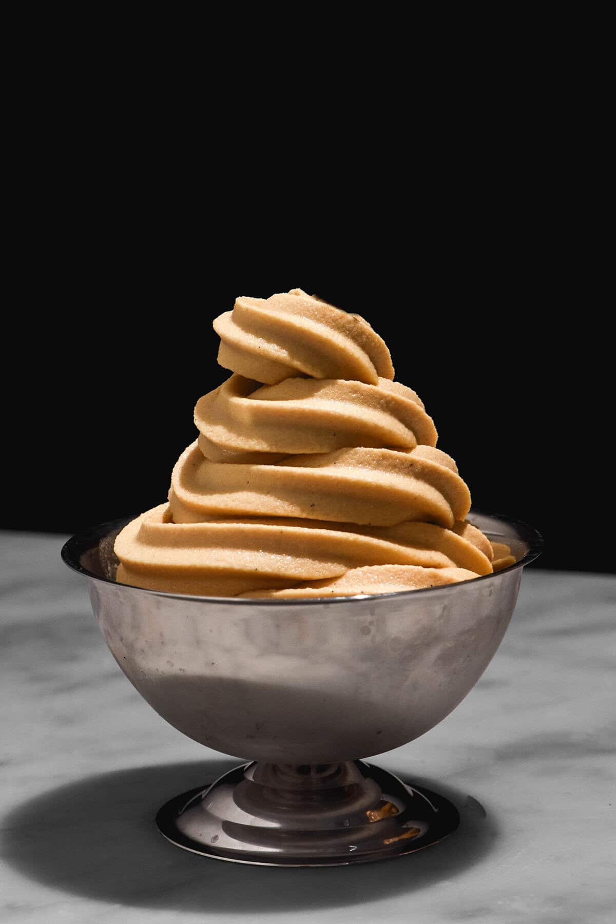A moody image of a Ninja Swirl coffee serve in a silver dessert coupe on a white marble table against a black backdrop