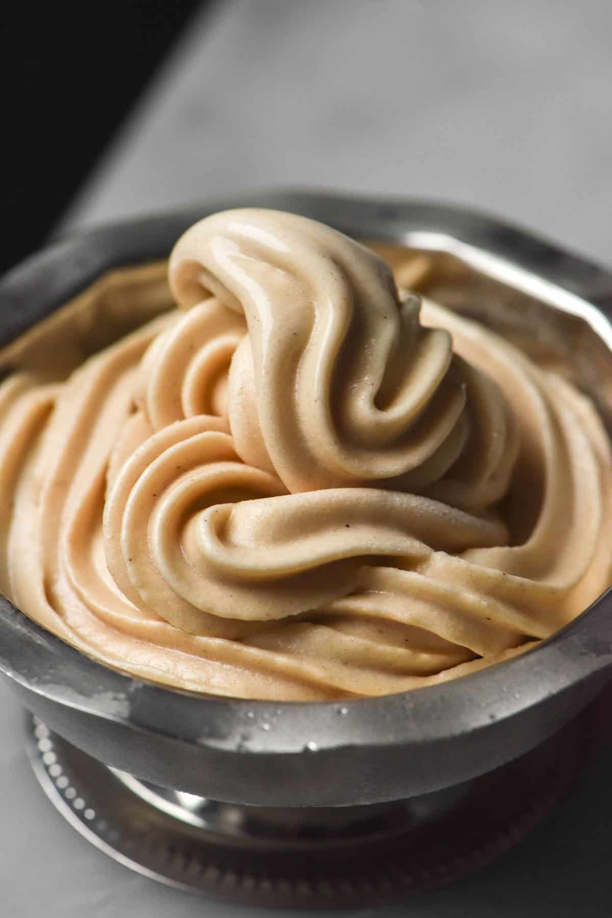 A macro close up image of Ninja Swirl high protein soft serve in a silver dessert coupe on a white marble table