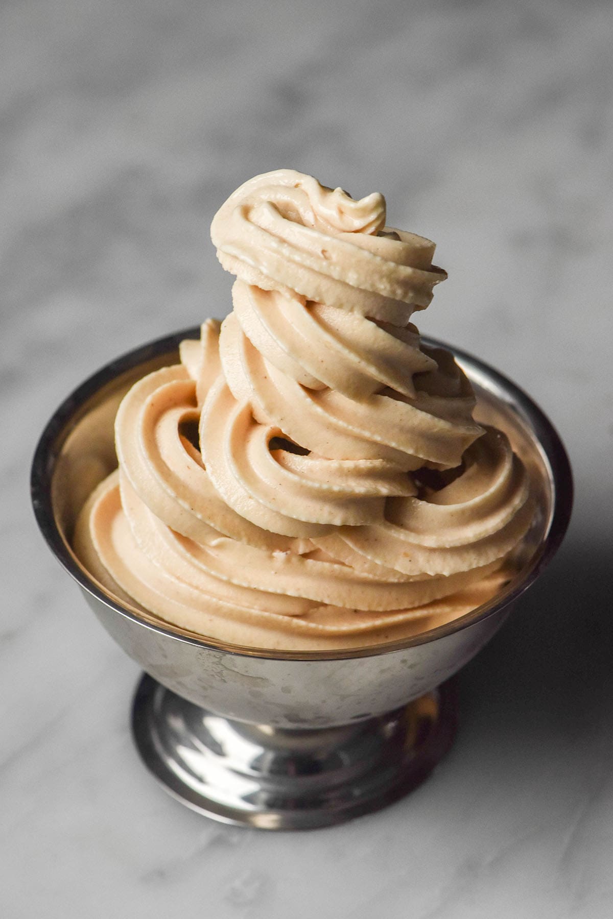 A side on image of a silver dessert coupe on a white marble table piled high with high protein Ninja Swirl soft serve