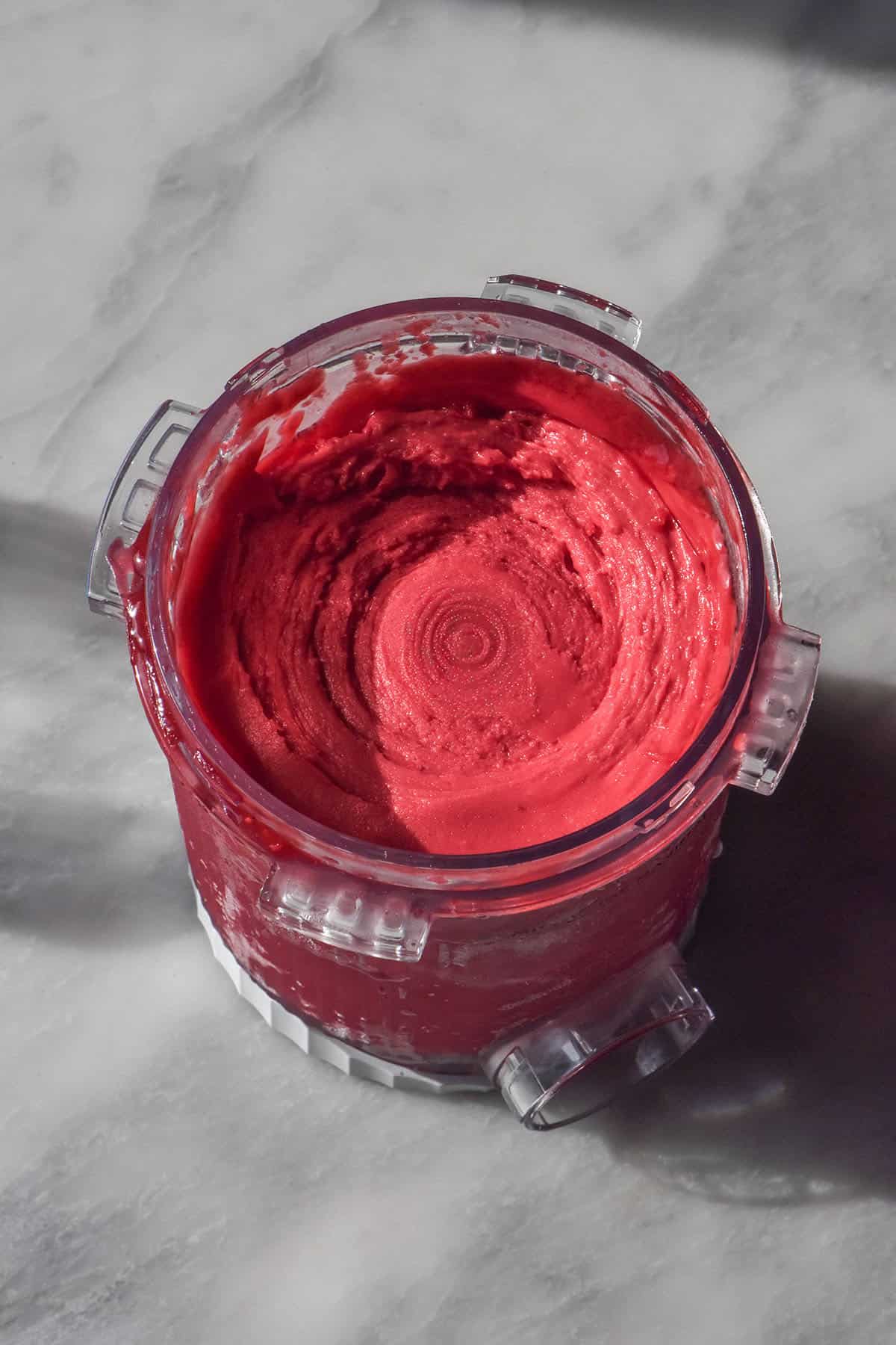 An aerial image of a tub of Ninja Swirl raspberry sorbet on a white marble table in bright sunlight