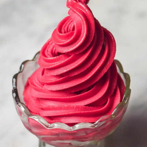 A side on image of a glass scalloped dessert coupe filled with Ninja Swirl raspberry sorbet on a white marble table