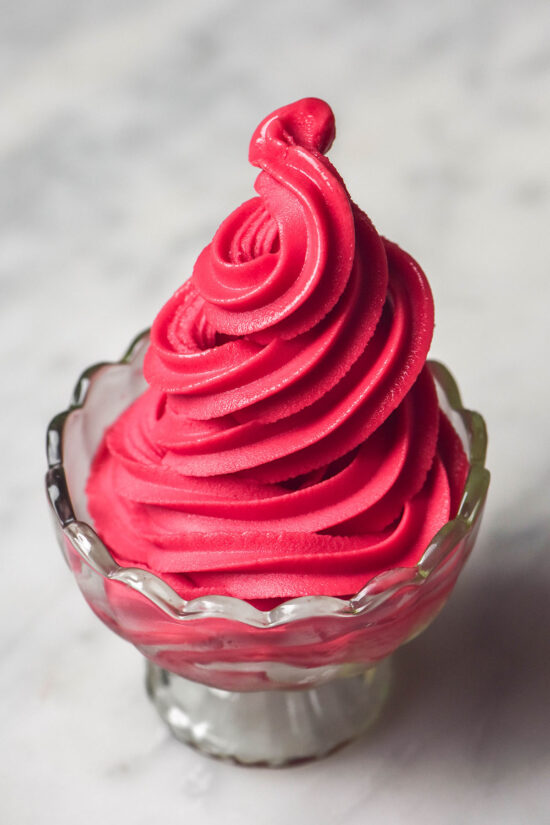 A side on image of a glass scalloped dessert coupe filled with Ninja Swirl raspberry sorbet on a white marble table