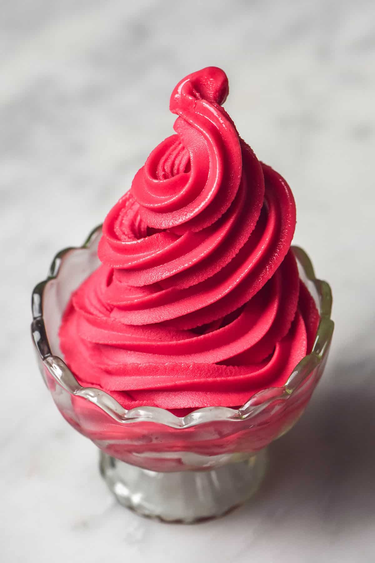A side on image of a glass scalloped dessert coupe filled with Ninja Swirl raspberry sorbet on a white marble table