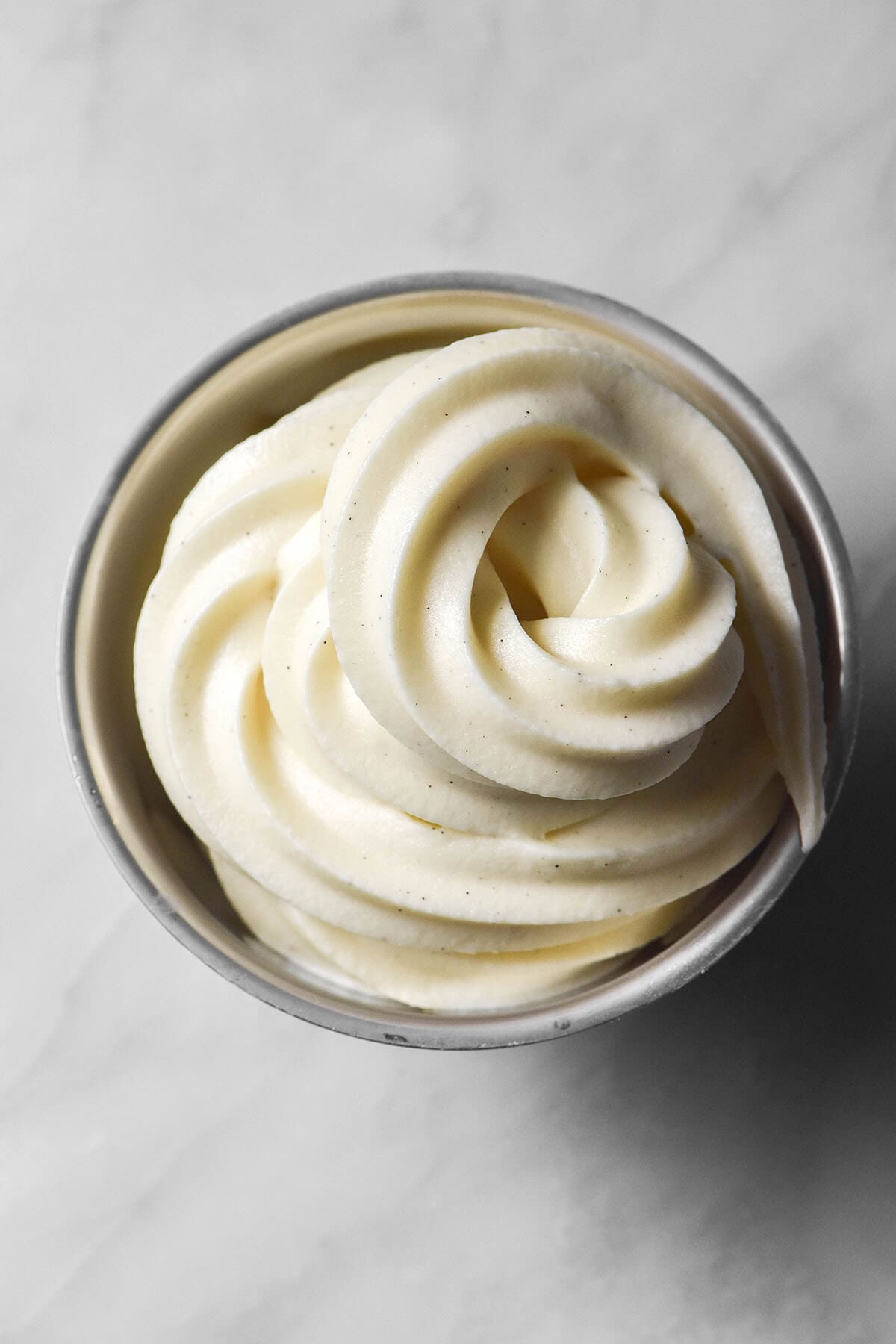 An aerial image of a swirl of Ninja Creami vanilla soft serve in a silver dessert coupe on a white marble table