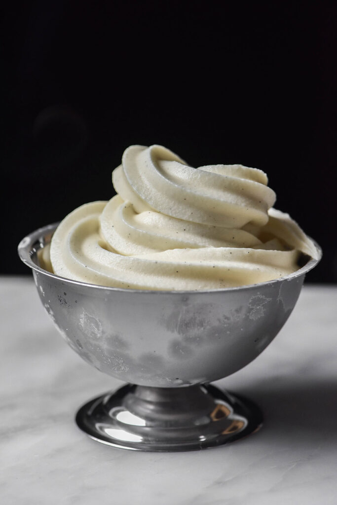 An side image of Ninja Swirl vanilla soft serve in a frozen dessert coupe on a white marble table against a black backdrop