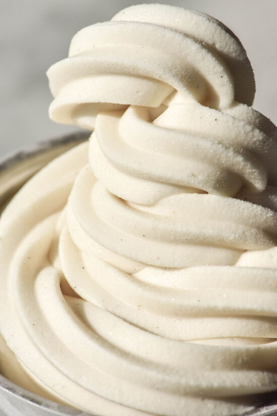 A close up macro image of a swirl of vegan vanilla soft serve against a white backdrop