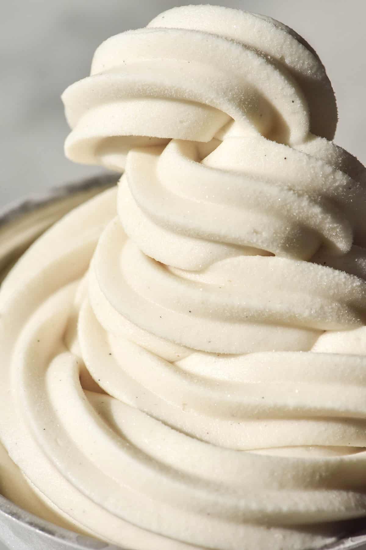 A close up macro image of a swirl of vegan vanilla soft serve against a white backdrop