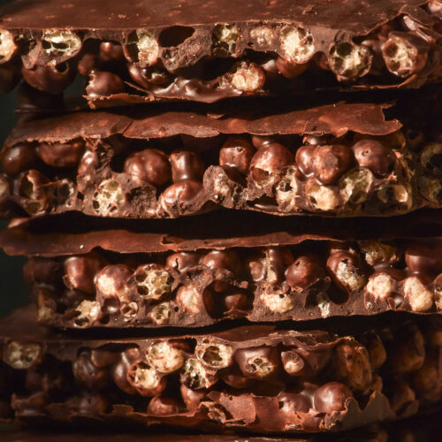 A macro close up side on view of a stack of protein crisp chocolate against a dark backdrop