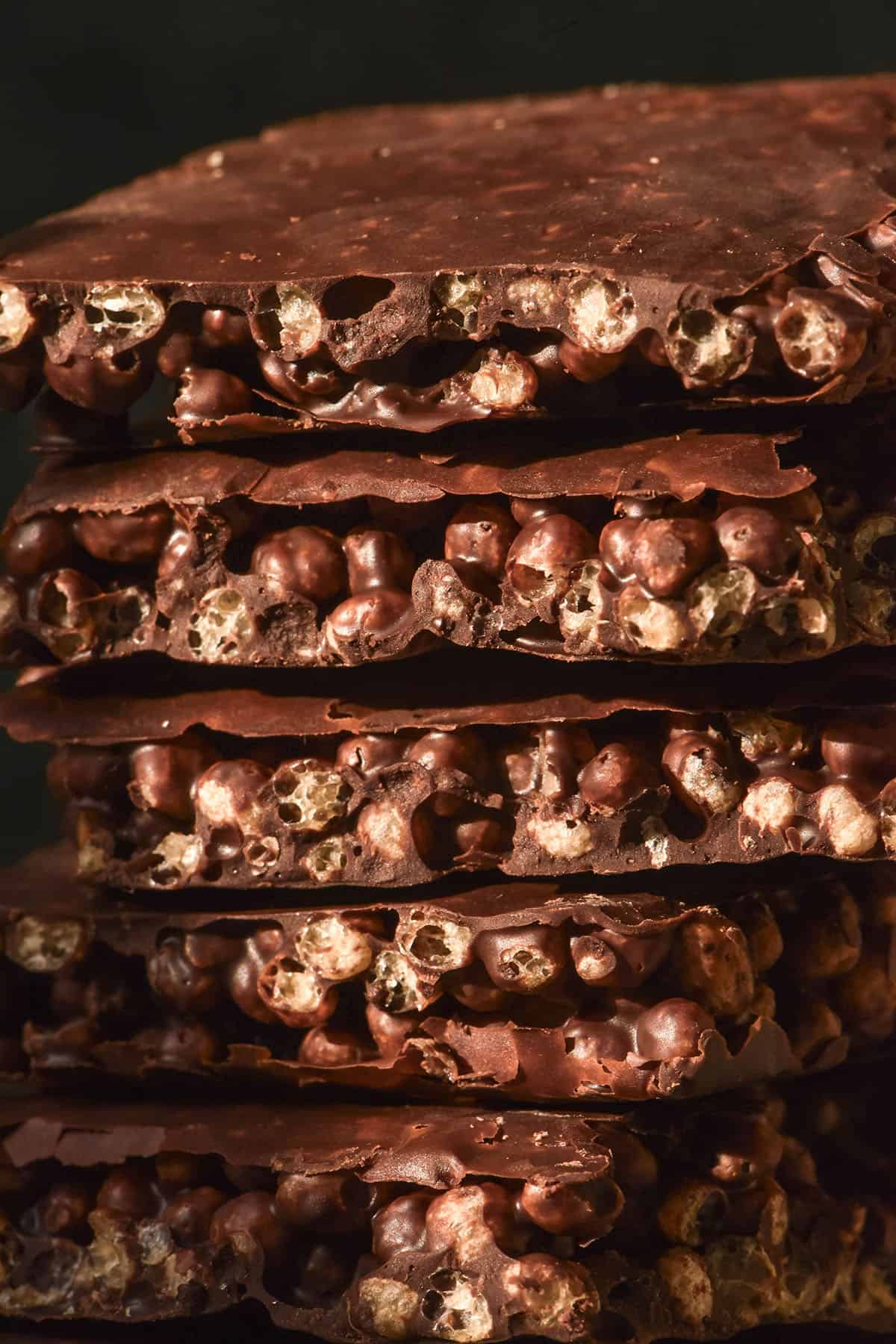 A macro close up side on view of a stack of protein crisp chocolate against a dark backdrop