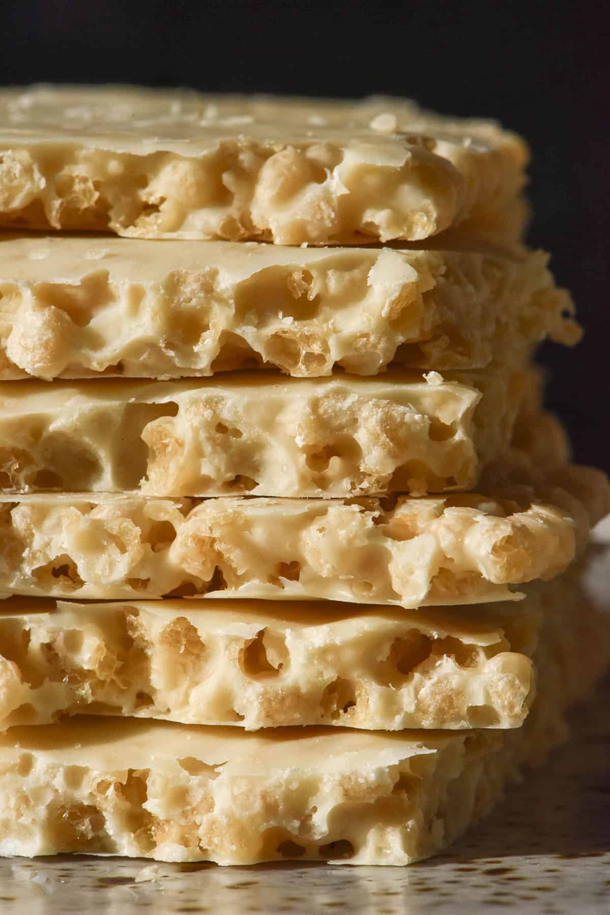 A side on macro image of a stack of white chocolate protein crisp on a white speckled ceramic plate against a dark backdrop