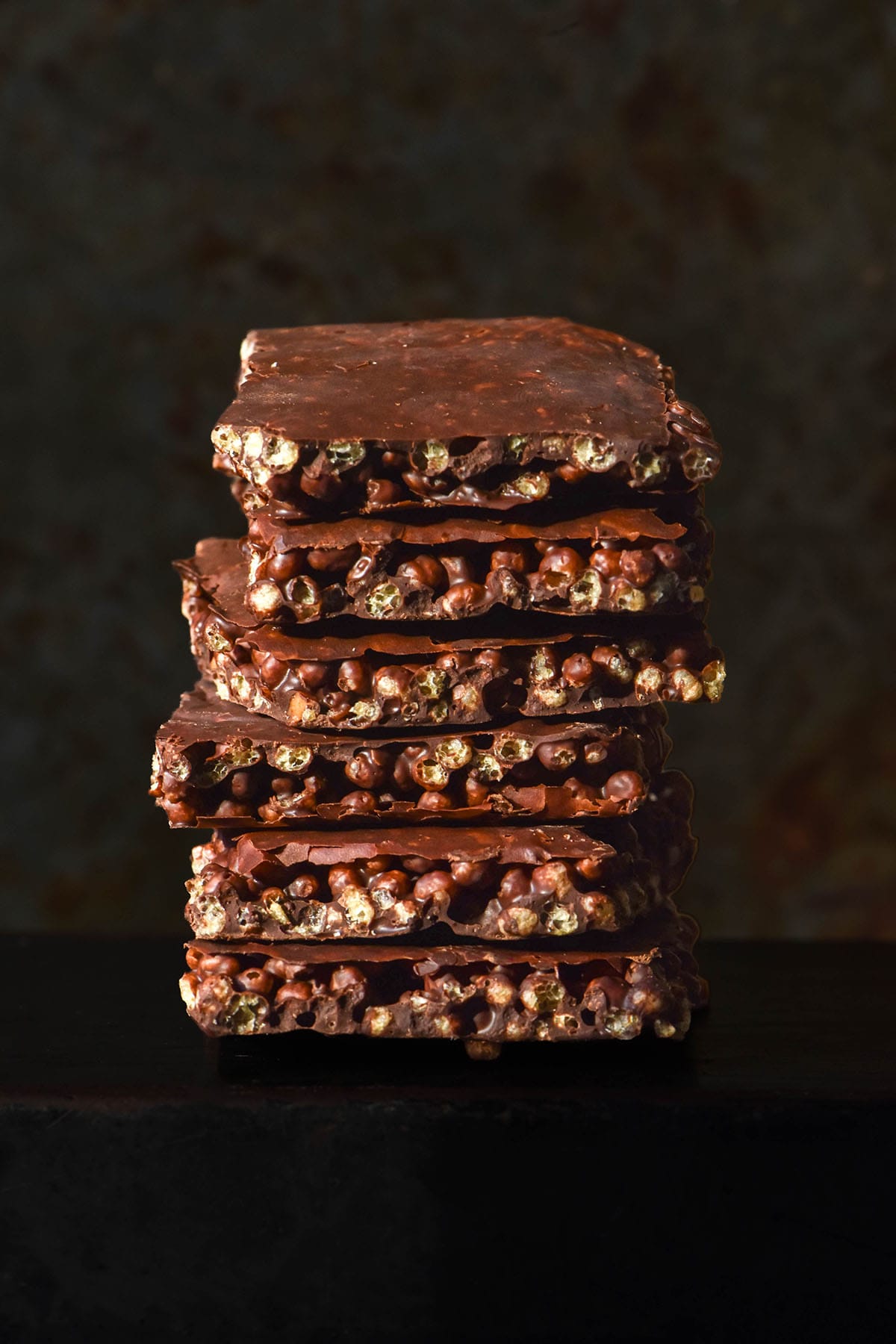 A side on image of a stack of protein crisp chocolate on a dark surface against a dark backdrop