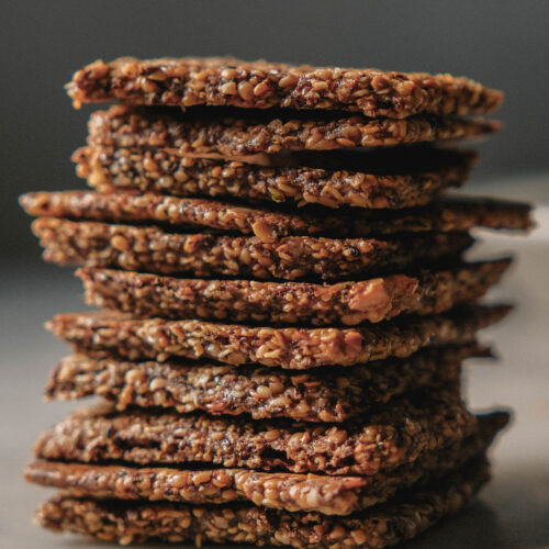 A side on image of high protein crackers in a stack on a white ceramic table against a dark backdrop